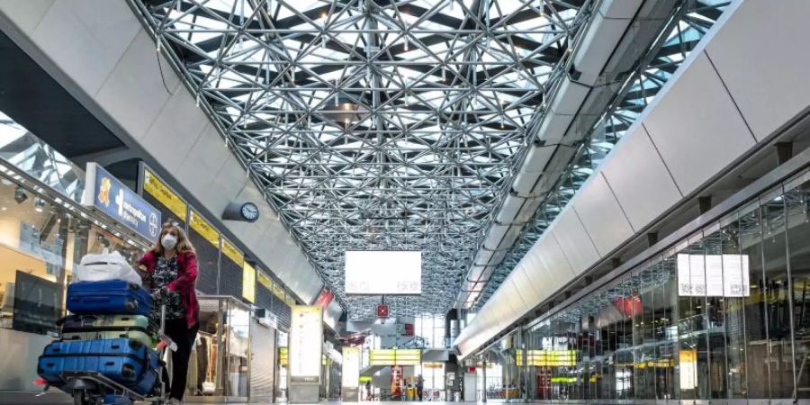 Eine Frau mit Mundschutzmaske läuft durch die ansonsten leere Haupthalle des Flughafens Tegel. Foto: Fabian Sommer/dpa