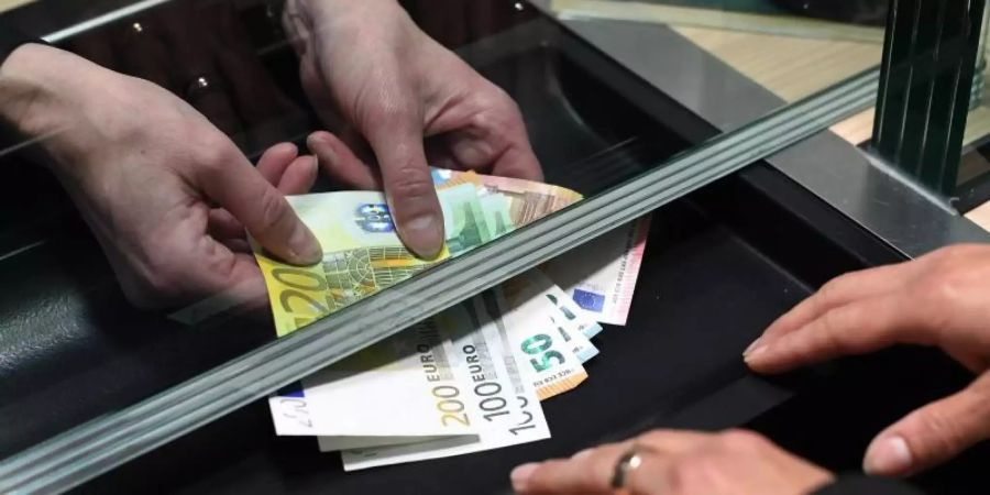 Eine Frau lässt sich in einer Bankfiliale am Schalter Bargeld auszahlen. Foto: Angelika Warmuth/dpa