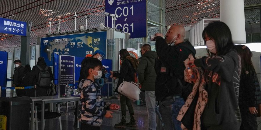 Passagiere mit Mund-Nasen-Schutz stehen am Flughafen Peking an der Sicherheitskontrolle vor einem internationalen Abfluggate an.
