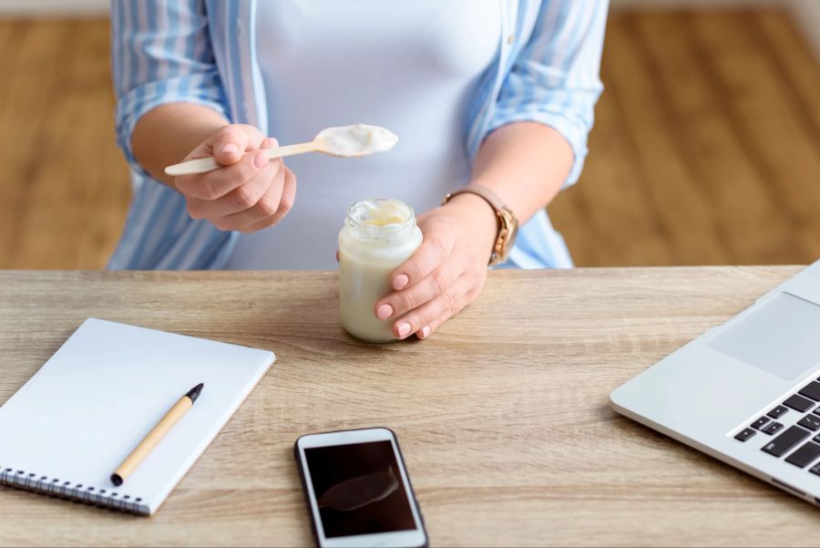 Frau isst Joghurt am Schreibtisch