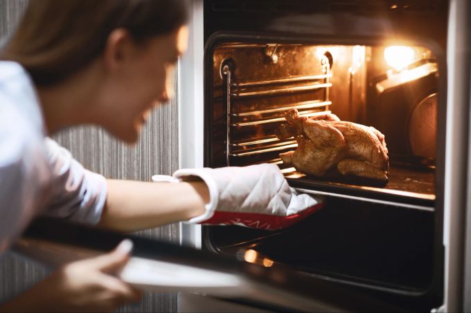 Wenn das rohe Huhn nicht auffällig riecht und keine Flüssigkeit absondert, ist es üblicherweise noch gut. Frau holt Huhn aus dem Ofen