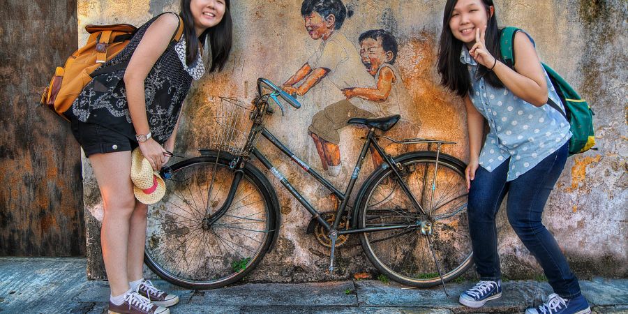 Zwei asiatische Mädchen vor dem Wandgemälde "Zwei Kinder auf dem Fahrrad".