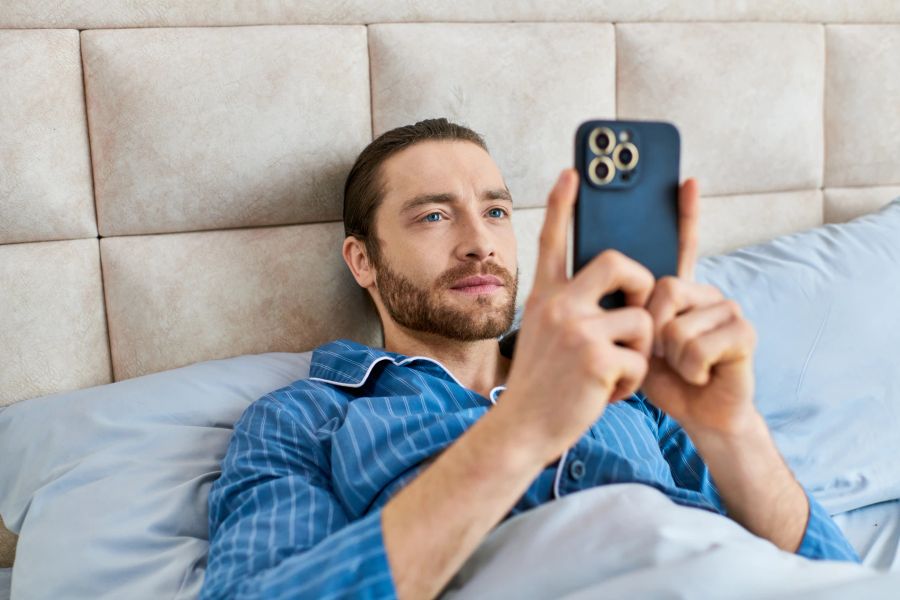 Mann liegt im Bett und schreibt auf seinem Smartphone