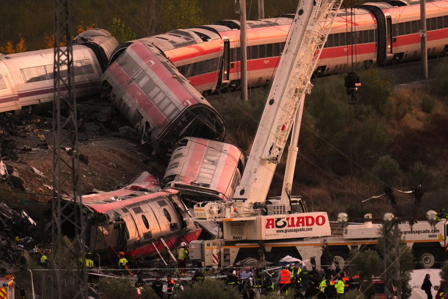 Der Kran steht direkt vor den umgestürzten Waggons. Rund um die Wracks arbeiten Einsatzkräfte der Guardia Civil und der Feuerwehr.