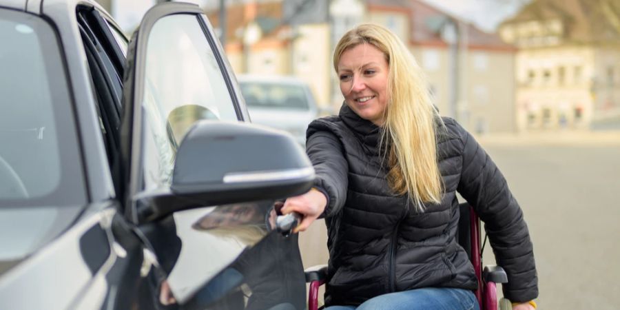 Frau im Rollstuhl öffnet Fahrertür am Auto