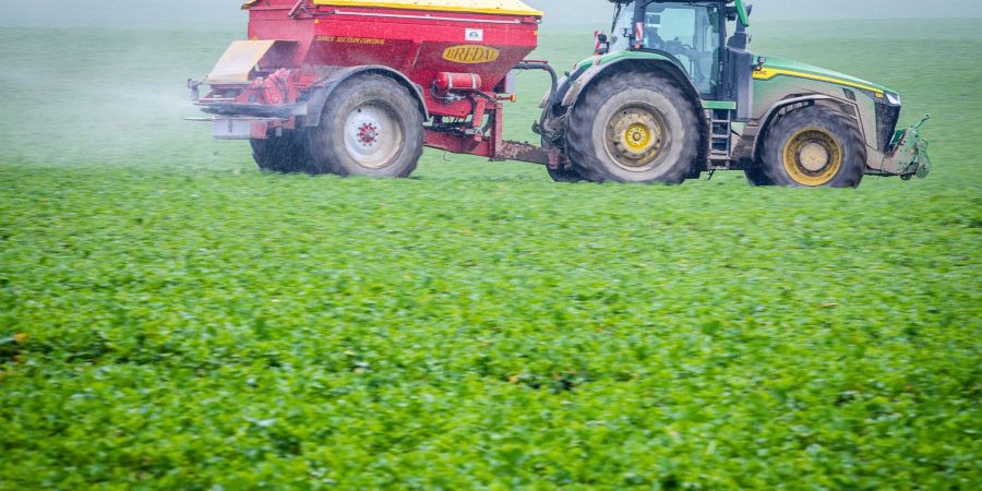 Ein Traktor fährt mit einem Streuwagen über ein Feld und bringt Dünger aus.