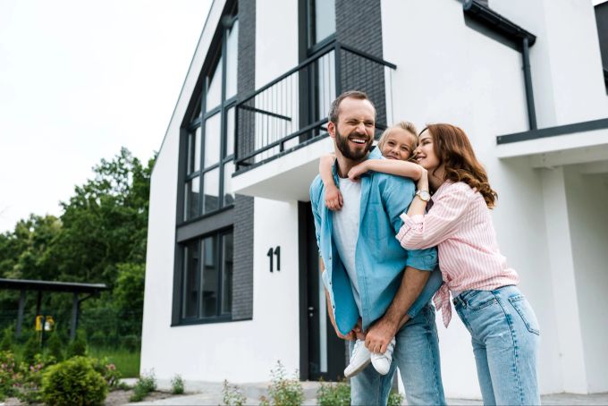 Es gibt viele Gründe für den Vermögensaufbau, zum Beispiel der Kauf einer Immobilie oder die Vorsorge für die Kinder. Familie vor Haus