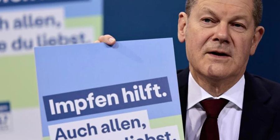 Bundeskanzler Olaf Scholz präsentiert ein Plakat aus der neuen Impfkampagne. Foto: Hannibal Hanschke/POOL AP/dpa
