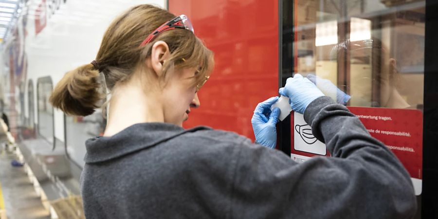 Eine SBB-Mitarbeiterin entfernt Aufkleber, die auf die Maskenpflicht im Zug aufmerksam machen. Seit Freitag müssen in der Schweiz im öffentlichen Verkehr wegen der Coronavirus-Pandemie keine Masken mehr getragen werden.
