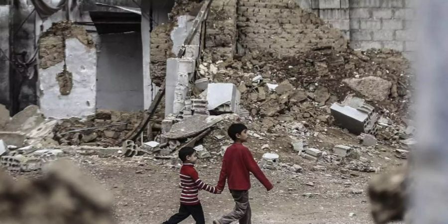 Zwei syrische Jungen gehen Hand in Hand an zerstörten Häusern vorbei. Foto: Mohammed Badra/epa/dpa