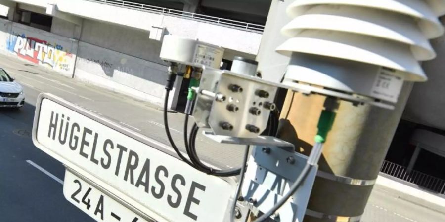 Autos fahren auf der Darmstädter Hügelstrasse an einer Luftmessstation vorbei. Foto: Arne Dedert/dpa