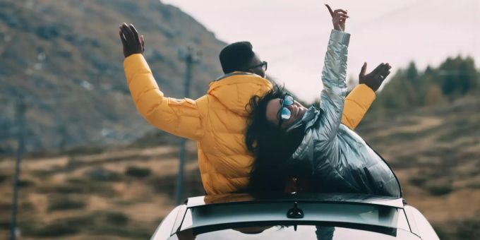 Zwei junge Leute stehen im Auto, ragen mit ihren Oberkörpern aus dem Dachfenster und geniessen das Leben. SunIce Festival