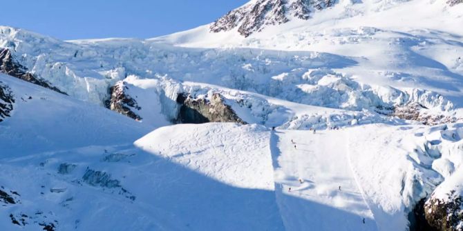 Skifahrer und Snowboarder fahren in Saas-Fee auf einer Piste.