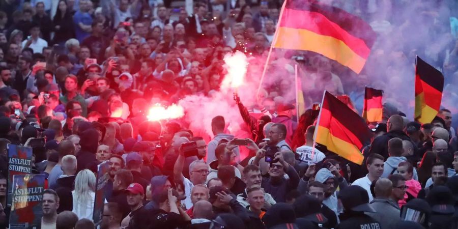 Demonstranten der rechten Szene zünden Pyrotechnik und schwenken Deutschlandfahnen.