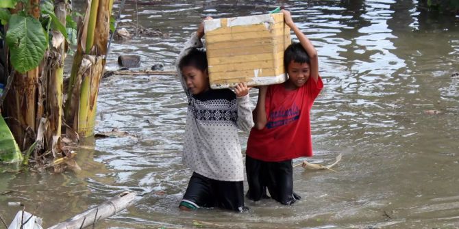 Kinder waten mit einer geschulterten Kiste im Wasser