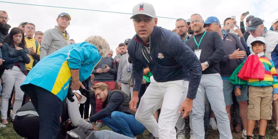 Brooks Koepka (M) vom Team USA kommt zu einer Zuschauerin, die von seinem Golfball getroffen wurde, und nun am Boden liegt, am ersten Tag des Turniers in Saint-Quentin-en-Yvelines bei Paris.