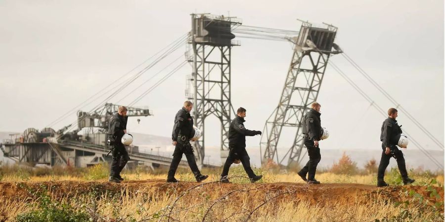 Polizisten gehen am Hambacher Forst vor einem Braunkohlebagger des Tagebaus Hambach vorbei.