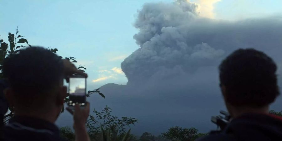 Einwohner von Bali beobachten die imposante Rauchsäule über dem Mount Agung.