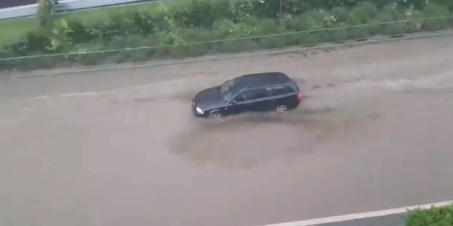 Eine Strasse in Sitten ist überflutet. Trotzdem kämpft sich ein Auto gegen die Wassermassen an.