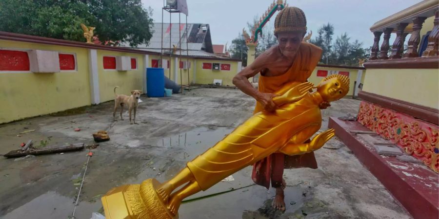 Ein buddhistischer Mönch richtet eine Buddha-Statue wieder auf.