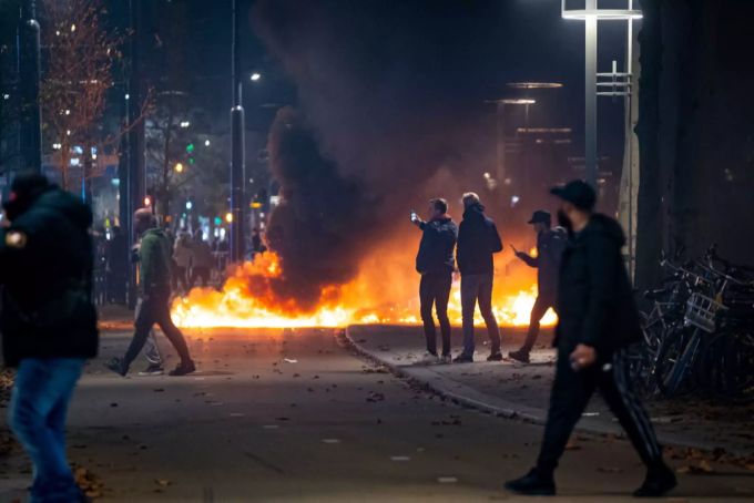 Menschen stehen neben einem Brand bei den Krawallen in Rotterdam. Rotterdam