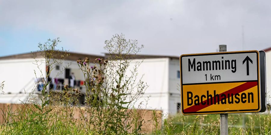 Das Ortsschild von Mamming, im Hintergrund sind die Unterkünfte von Erntehelfern zu sehen. Foto: Armin Weigel/dpa