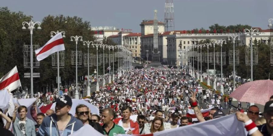 Demonstranten marschieren mit der ehemaligen belarussischen Nationalflagge in den Händen auf der Strasse. Foto: Uncredited/AP/dpa