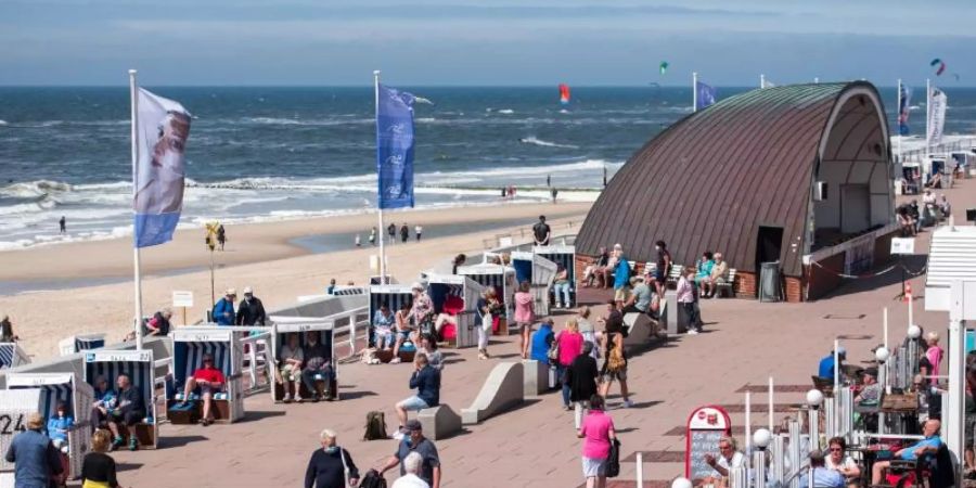 Passanten sind auf der Nordseeinsel Sylt am Strand in Westerland auf der Promenade unterwegs. (Archivbild). Foto: Daniel Bockwoldt/dpa