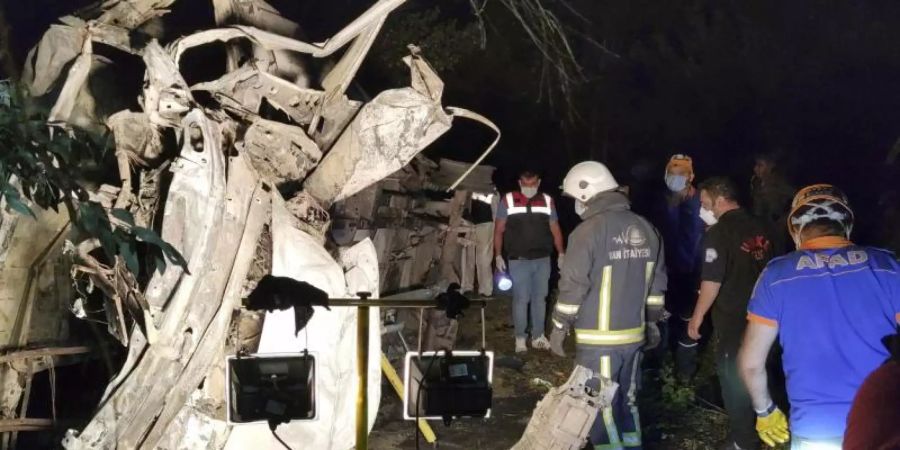 Rettungskräfte stehen neben einem ausgebrannten Wrack eines Kleinbusses, der beim Transport von Migranten in einen Graben gestürzt und dann in Brand geraten sein soll. Foto: Sukru Akyuz/IHA/AP/dpa