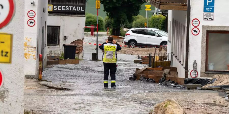 Ein Feuerwehrmann steht auf einer überfluteten Strasse in Bayern.