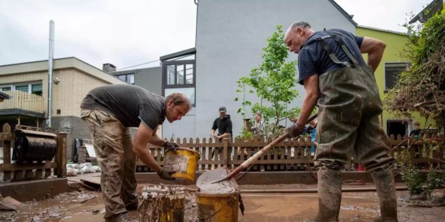 Mit Eimern entsorgen Anwohner die Schlammmassen nach dem Hochwasser der Kyll. Zahlreiche Häuser im Ort waren betroffen, Bewohner mussten evakuiert werden. Foto: Harald Tittel/dpa