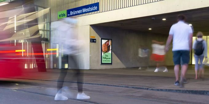 Blick auf die BLS-Station Westide-Brünnen. Werbescreen bei Bahnhof