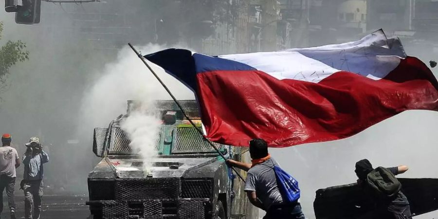 Flagge und Wasserwerfer: Momentaufnahme eines Protests in Chile gegen soziale Ungleichheit und die Regierung. Foto: Pablo Ovalle Isasmendi/Agencia Uno/dpa