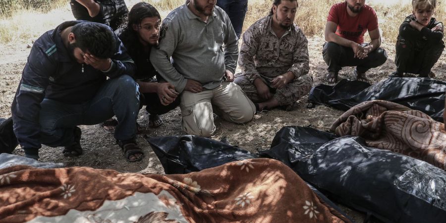 Trauernde sitzen 2021 neben eingehüllten Leichen unter Bäumen in Idlib und warten darauf, dass Kampfflugzeuge abziehen.