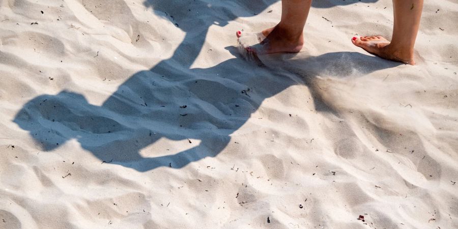 Eine Frau geht mit nackten Füssen durch den warmen Sand.