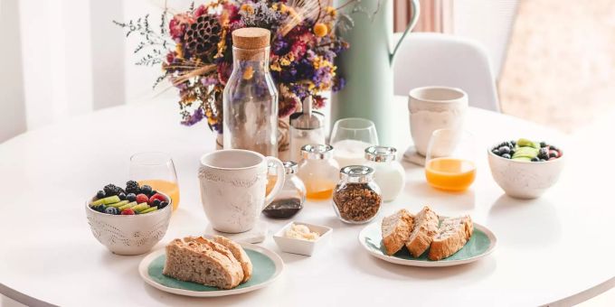 Auf einem Tisch ist ein Frühstück mit Brot, Früchten, Tee und Orangensaft angerichtet. Frühstück