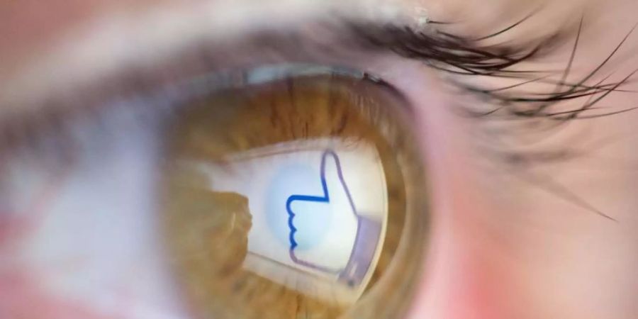 Ein nach oben zeigender Daumen (Facebook-Logo für «gefällt mir») spiegelt sich im Auge des Betrachters. Foto: Friso Gentsch/Illustration