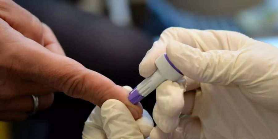 Ein Arzt nimmt an dem Finger eines jungen Mannes Blut ab. In vielen Ländern ist die Zahl der HIV-Tests in der Pandemie zurückgegangen. Foto: Britta Pedersen/dpa-Zentralbild/dpa
