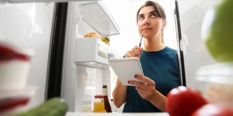 Frau vor Kühlschrank schreibt Einkaufsliste