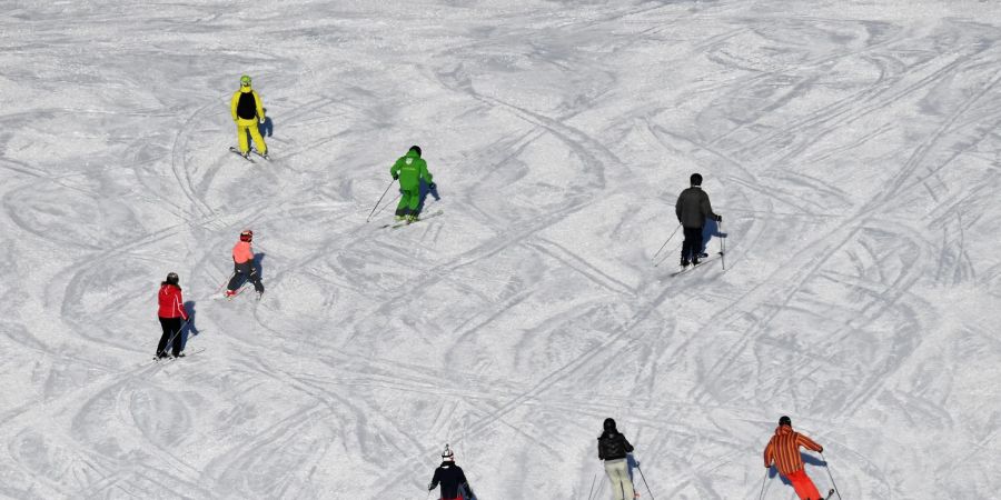 Skifahrer fahren bei Sonnenschein auf einer Skipiste.