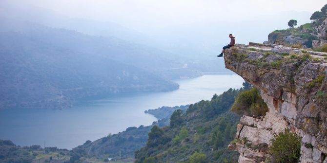 mann sitzt allein auf einer klippe, fluss, fjordlandschaft
