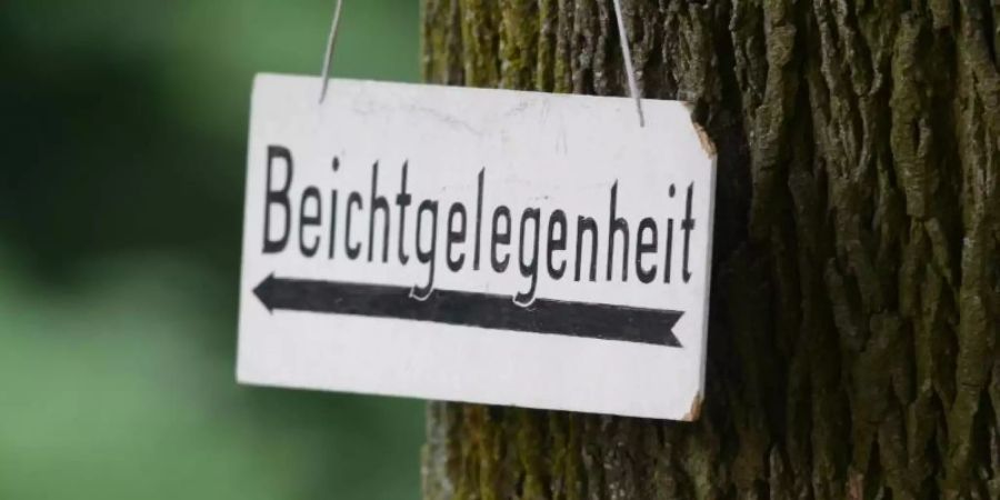 Ein Schild mit der Aufschrift «Beichtgelegenheit» hängt an einem Baum. Foto: Armin Weigel/Illustration