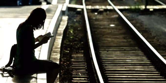 Eine Frau sitzt lesend an einem Bahngleis auf dem Perron. Das Einkommen hat weniger Einfluss als angenommen.