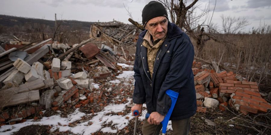 Andrii Cherednichenko (50), der von einer Landmine verletzt wurde, steht auf Krücken vor den Ruinen seines Hauses im ukrainischen Kamjanka.