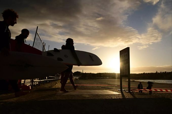 Surfer gehen am Bondi Beach mit ihren Surfbrettern zum Wasser. Der Strand, der wegen des Coronavirus vorübergehend geschlossen war, ist für die Öffentlichkeit wieder geöffnet. Coronavirus - Australien