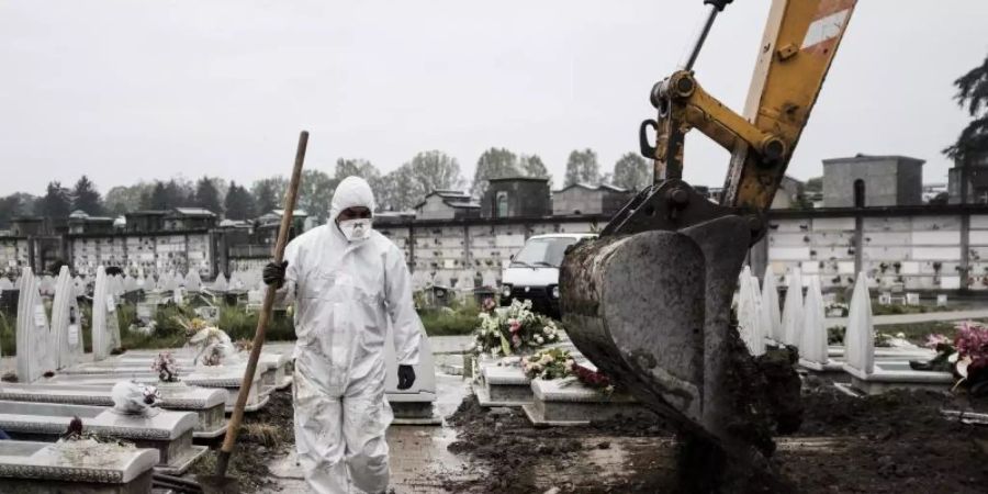 Ein Mitarbeiter im Schutzanzug geht in der Industriestadt Turin über einen Friedhof, auf dem frische Gräber ausgehoben werden. Foto: Marco Alpozzi/LaPresse via ZUMA Press/dpa