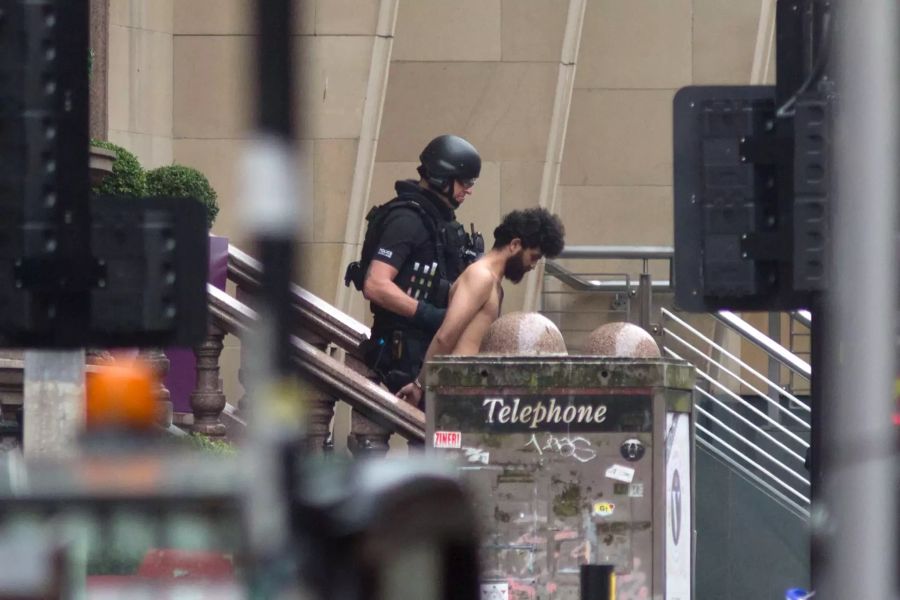 Ein Polizist führt einen Mann in Handschellen am Tatort in Glasgow ab.