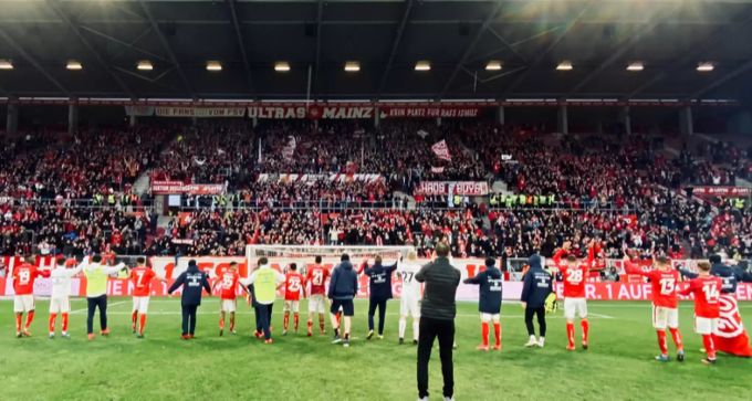 Die Spieler des 1. FSV Mainz 05 jubeln vor der Fankurve. Oberhalb der Fans ist ein Banner mit der Aufschrift «Kein Platz für Rassismus» zu sehen. 1. FSV Mainz 05