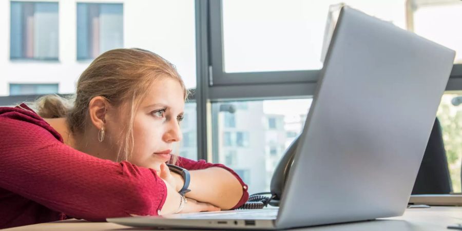 Frau vor Computer auf Schreibtisch mit Armen liegend