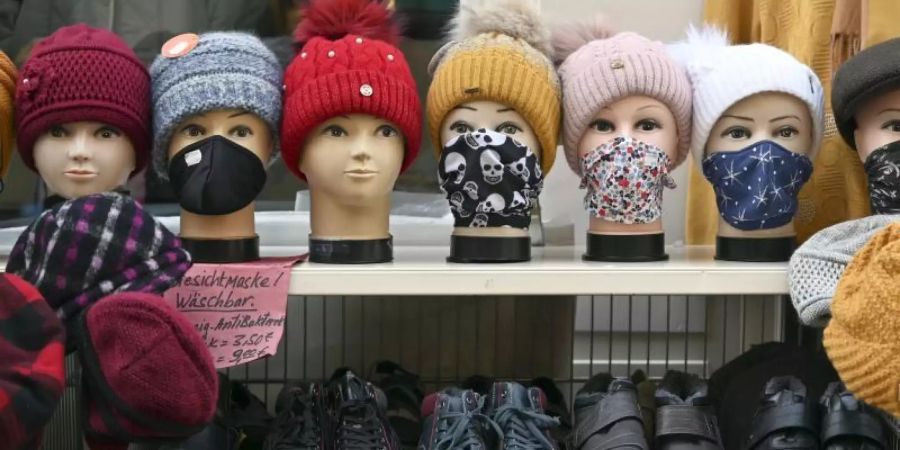 Schaufensterpuppenköpfe mit Gesichtsmasken, Tüchern und Mützen stehen vor einem Bekleidungsgeschäft in der Altstadt von Mühlhausen. Foto: Martin Schutt/dpa-Zentralbild/dpa